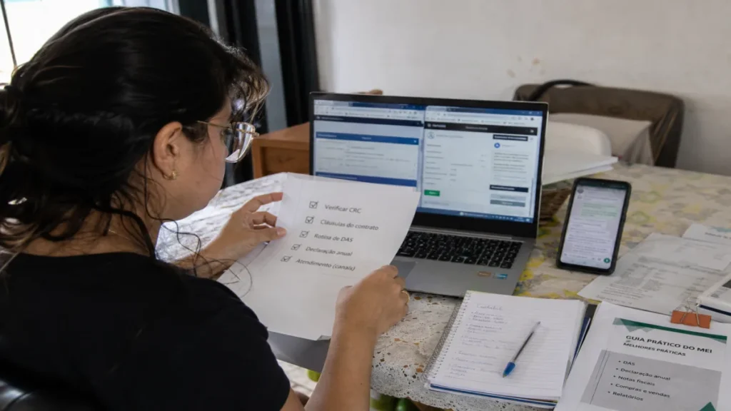 Microempreendedor analisa propostas de contador online para MEI no notebook, com checklist e documentos organizados